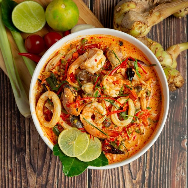 Spicy seafood soup with shrimp, squid, and mussels, garnished with lime and chili.