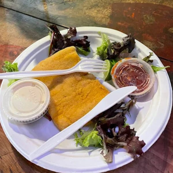 Fried fish fillets with mixed greens, lime, and dipping sauces on a white paper plate.