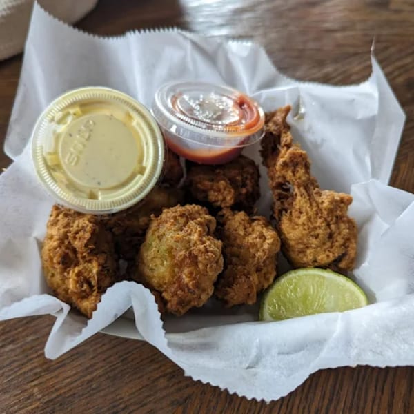B.O.'s Fish Wagon conch fritters with two dipping sauces and a lime wedge in a paper-lined basket.