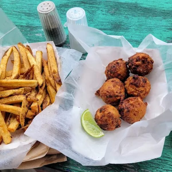 Fried fish fritters with a lime wedge and french fries on a teal wooden table.