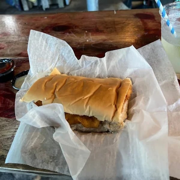 A B.O.'s Fish Wagon fried fish sandwich wrapped in paper, with a drink and sauce.